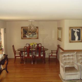 A cozy dining room with a wooden table and chairs, adorned with artwork on the walls and a polished wooden floor.