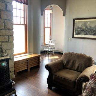 A cozy living room featuring a comfortable armchair, a stone fireplace, and large windows that allow ample natural light.