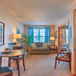 A cozy living room with a sofa, table, chairs, and a large window with blue curtains.