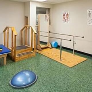 A physical therapy room equipped with rehabilitation tools, including stairs, parallel bars, and a balance ball.