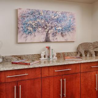 A kitchen area featuring wooden cabinets with a granite countertop, adorned with decorative items and a tree-themed artwork on the wall.
