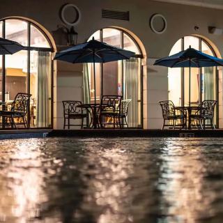 A serene evening view of an outdoor seating area with umbrellas, reflected in a nearby water surface.