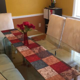 A dining room with a glass table adorned with a colorful table runner and a vase of flowers.