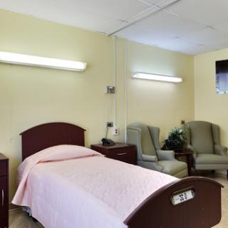 A hospital room featuring a bed with a pink cover and two chairs.