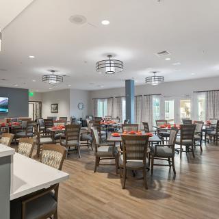 A spacious and modern dining room with multiple tables and chairs, featuring stylish light fixtures and large windows.