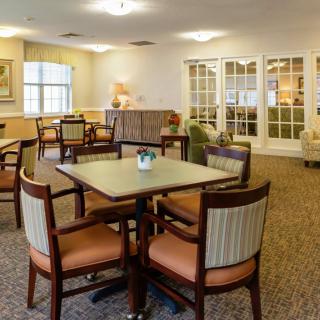 A cozy dining area with tables and chairs arranged on a carpeted floor, illuminated by overhead lighting.
