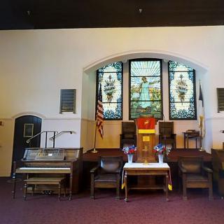 Interior of a church featuring stained glass windows, an altar, and an organ.