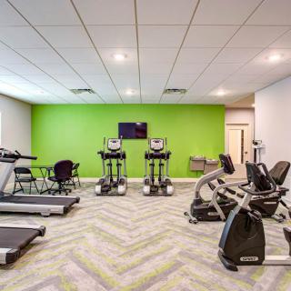 A modern gym with various exercise equipment, including treadmills and stationary bikes, against a vibrant green accent wall.