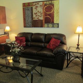 A cozy living room with a leather sofa, glass coffee table, and decorative artwork on the wall.