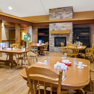 A cozy dining area featuring wooden tables and chairs, centered around a warm fireplace.