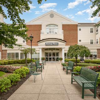 A welcoming entrance to a residential building, surrounded by lush greenery and seating areas.