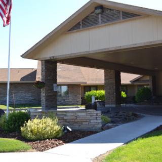 A welcoming entrance to a community building, featuring landscaped greenery and an American flag.