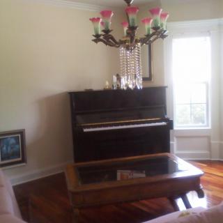 A cozy living room with a piano and chandelier.