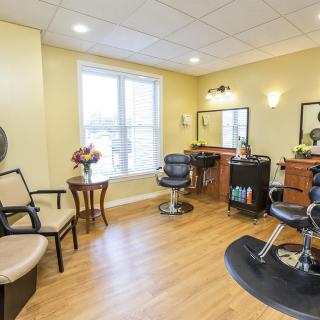 A cozy hair salon with comfortable chairs and mirrors, adorned with flowers and a large window letting in natural light.
