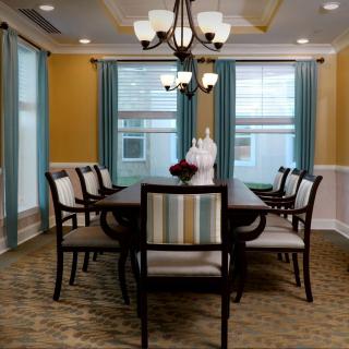 A well-furnished dining room with a large table, surrounded by chairs, under an elegant chandelier.