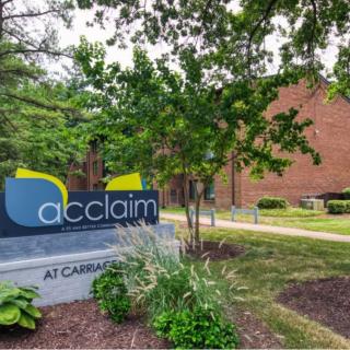 A landscaped entryway with a sign for 'acclaim' at an apartment complex.