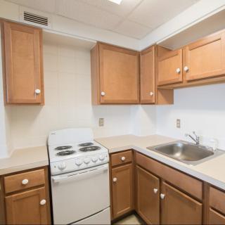 A compact kitchen with wooden cabinets, a small stove, and a sink.