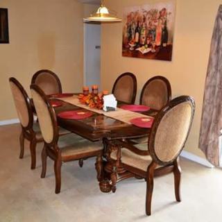 A classic dining room with a wooden table and upholstered chairs, decorated with a central runner and artwork on the wall.