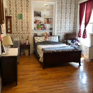 A cozy bedroom with a bed, bookshelf, and red curtains.