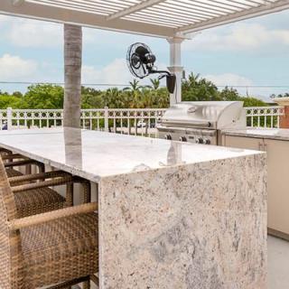 An elegant outdoor kitchen with a marble countertop and a built-in barbecue grill under a pergola.