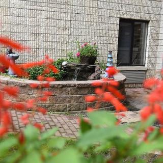 A charming garden area with vibrant red flowers and a brick planter against a building.