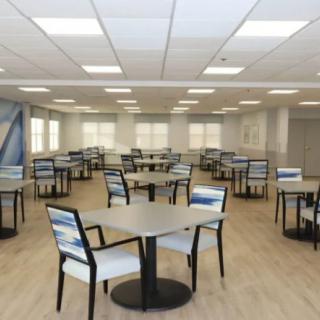 An empty cafeteria with neatly arranged tables and chairs, illuminated by overhead lighting.