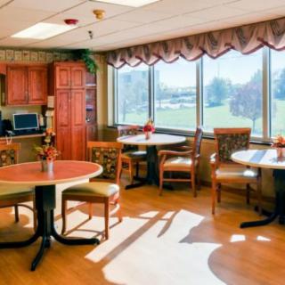 A cozy dining area with tables and chairs, bathed in natural light from large windows.