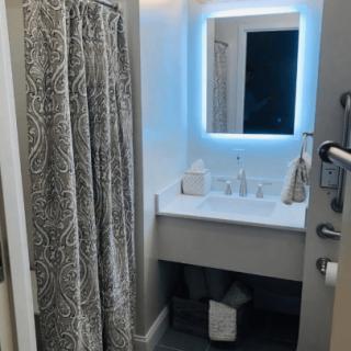 A modern bathroom with a well-lit mirror and shower curtain.