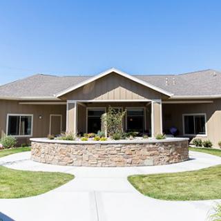 A modern residential building with a stone wall and landscaped front yard under a clear blue sky.