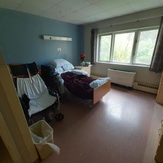 A view of a hospital patient room, featuring beds, chairs, and natural light from the window.