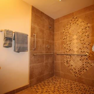 A modern walk-in shower with tiled walls and a handrail.