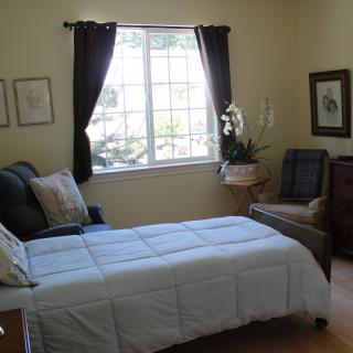 A cozy bedroom with a bed, armchair, and window featuring dark curtains.
