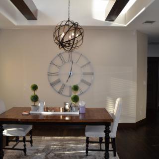 A modern dining room with a wooden table, unique chandelier, and decorative wall clock.