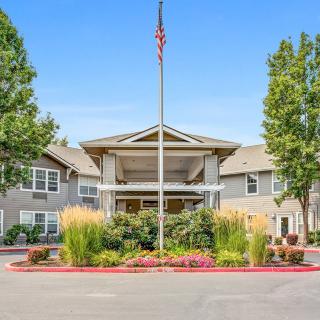 A well-maintained building entrance with a flagpole, surrounded by lush landscaping and trees.