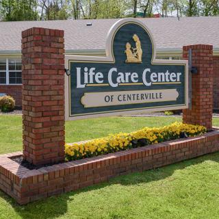 A sign for the Life Care Center of Centerville displayed in front of a brick structure with surrounding greenery.