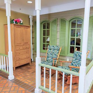 An indoor porch setup with green shutters, wooden rocking chairs, and a wooden cabinet.
