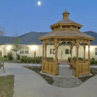 A wooden gazebo in front of a building under the evening sky with the moon visible.