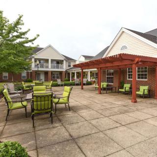 An outdoor patio area with green seating and a pergola, adjacent to residential buildings.