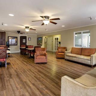 A spacious living room with wood flooring, furnished with sofas and chairs, and illuminated by ceiling fans.