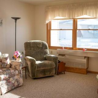 A cozy living room with sunlight streaming through the window, featuring an armchair and a floral chair.