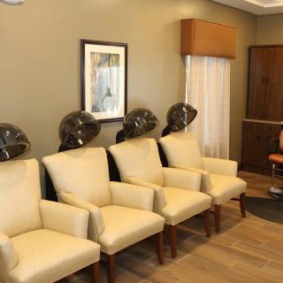 A cozy salon waiting area with cream-colored chairs and hair dryers lined up against the wall.