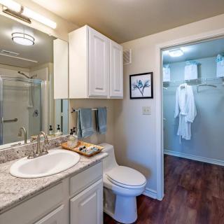 A clean and modern bathroom with a shower, sink, and toilet, featuring wooden floors and white cabinetry.