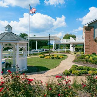 A serene garden with a gazebo, pathway, and American flag waving under a blue sky.