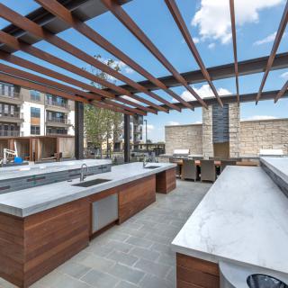 A modern outdoor kitchen with a pergola and spacious countertops, set in an urban environment.