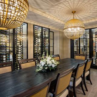 An elegant dining room with a luxurious wine cellar, chandeliers, and a long table adorned with flowers.