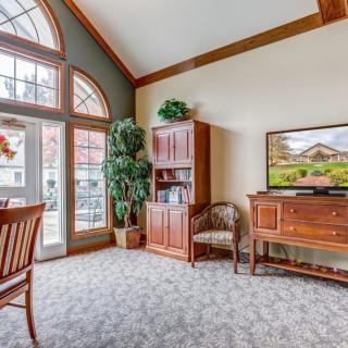 A cozy living room with large arched windows, wooden furniture, and a potted plant.
