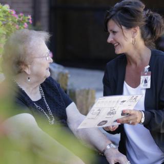 A caregiver converses with an elderly woman outdoors.