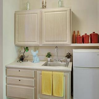 Small kitchen area with beige cabinets, a sink, refrigerator, and decorative items.
