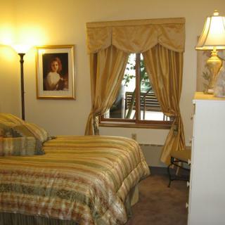 A cozy bedroom with a bed, a lamp, curtains, and a painting on the wall.