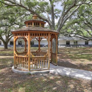 A wooden gazebo situated in a park, surrounded by large trees and a grassy area.